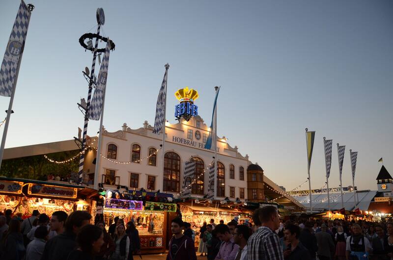 The Hofbräu-Festzelt at dusk, with blue-and-white flags and the crowd on the Wiesn in front of it.